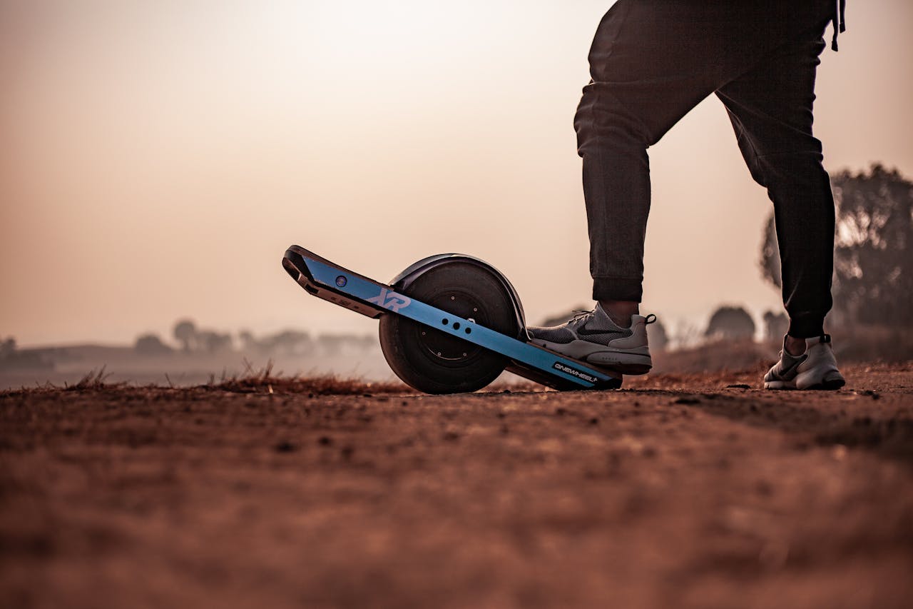 Close-up of a man standing on an electric unicycle during sunset on a dirt path.